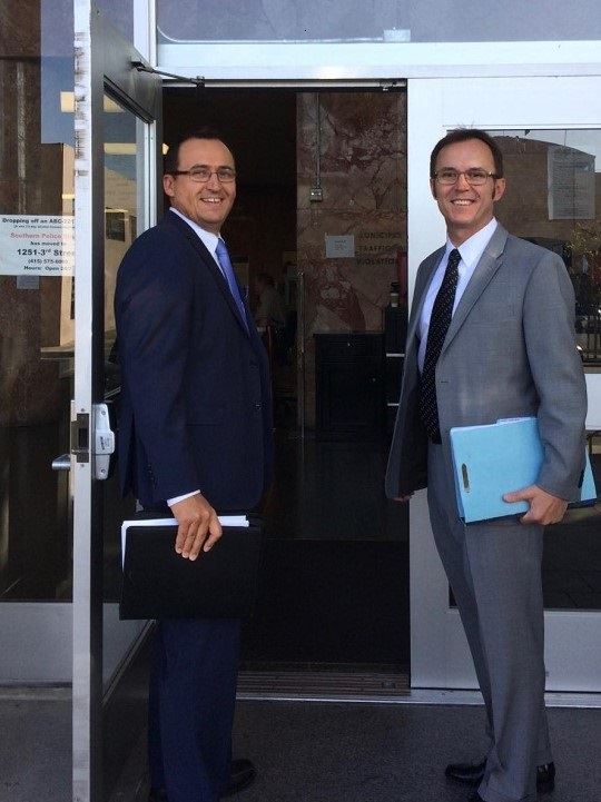 two men in suits standing in front of a glass door
