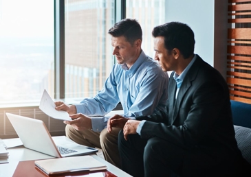 men sitting next to each other looking at a piece of paper
