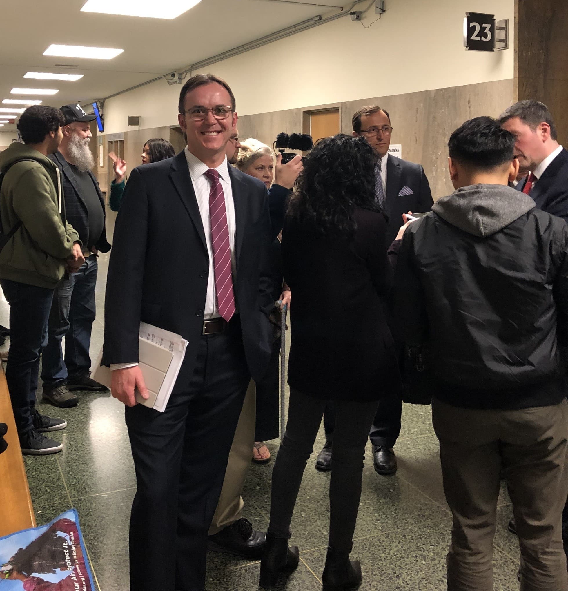 a man in a suit and tie standing in a hallway with other people
