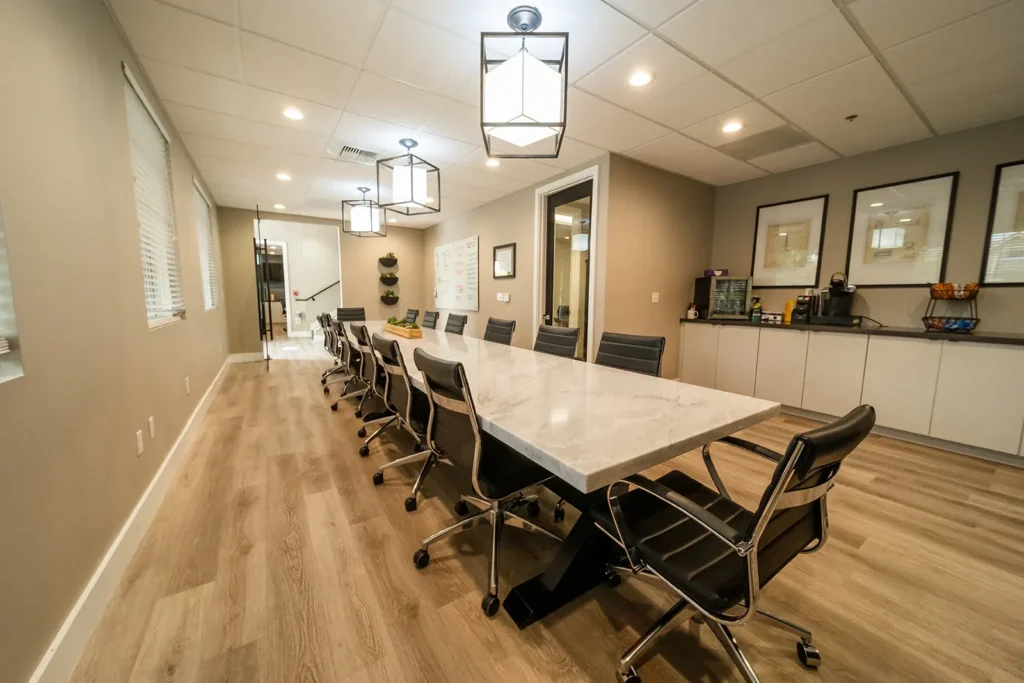Modern conference room with long marble table, black swivel chairs, pendant lights, and beige walls.