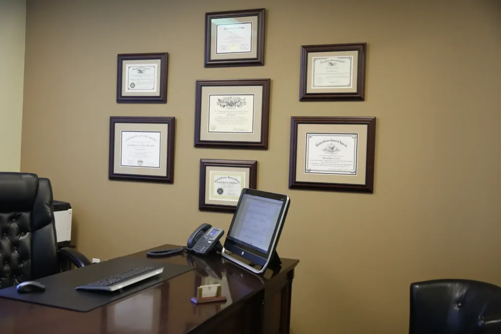 Professional office with dark wood desk, black leather chair, computer, phone, and framed certificates on beige wall.