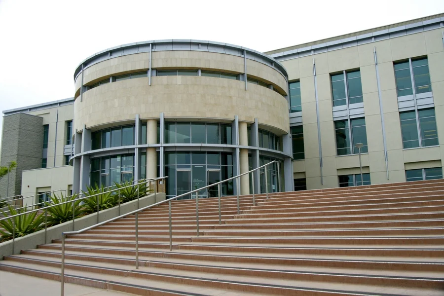Modern institutional building with wide brown steps, glass entrance, and beige exterior walls.